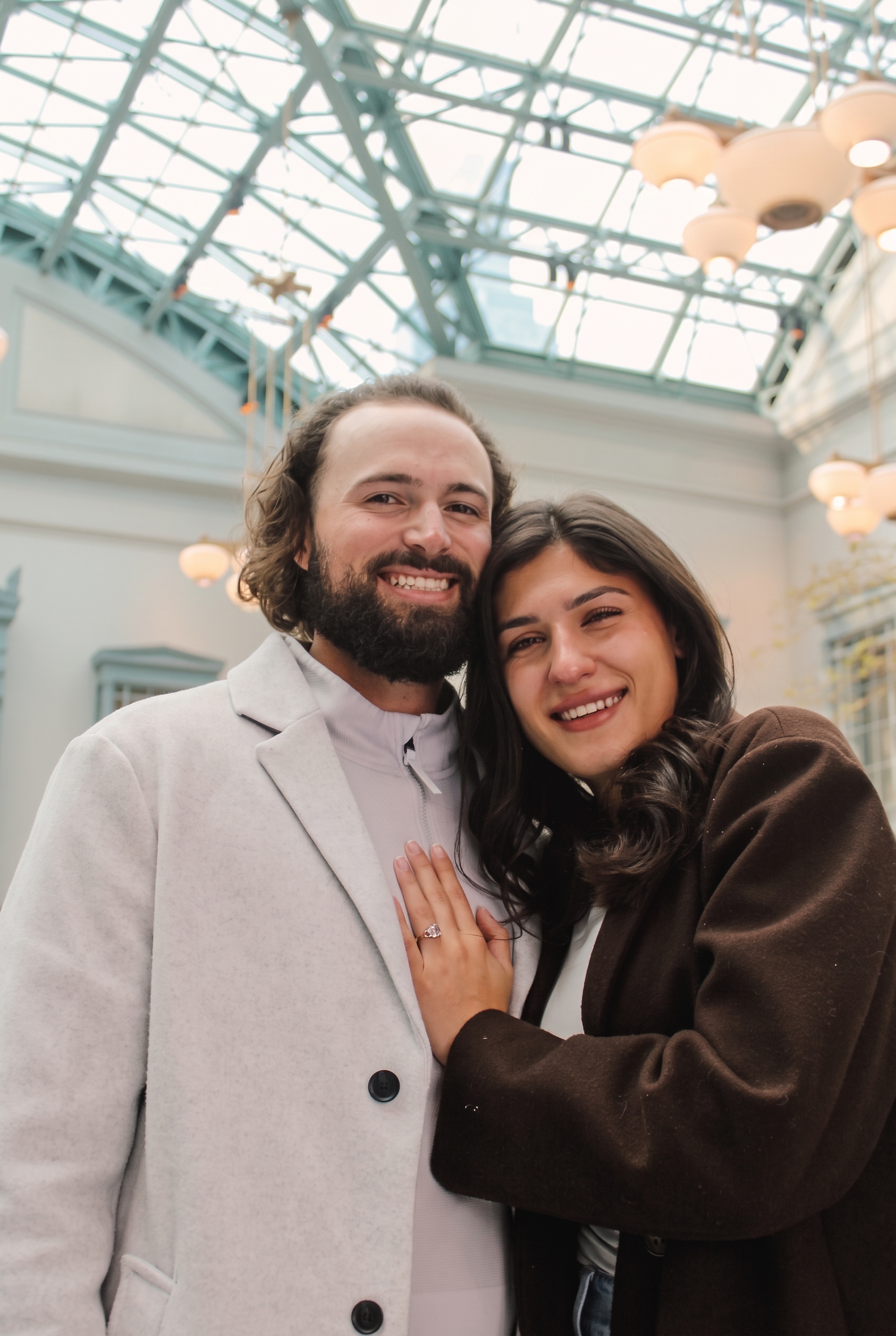Mariella resting her head against Nick beneath the atrium lights